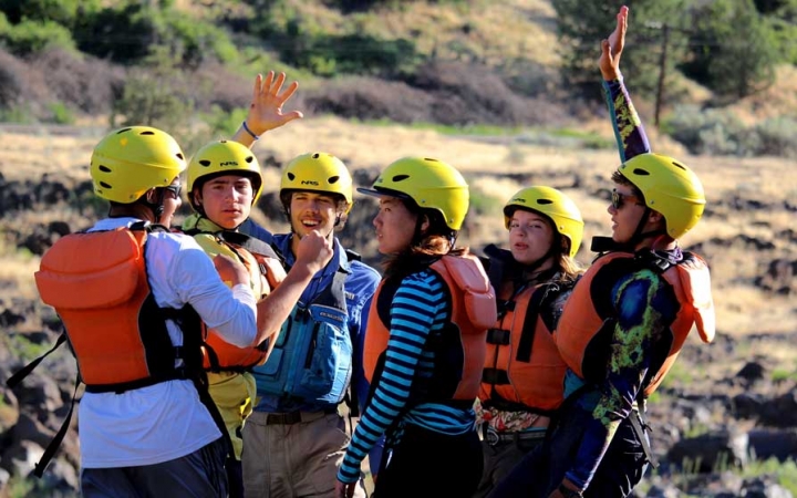 a group of students wearing life jackets and helmets stand and appear to celebrate by high-fiving 